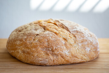 Fresh wheat homemade bread on the table. Shadows from the blinds are reflected on the wall. Morning, light background. Close-up