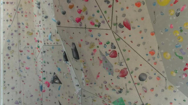 AERIAL: Flying around an empty indoor rock-climbing training center closed due to the covid-19 outbreak. Drone view of the high walls of a climbing gym filled with colorful magnesium-covered holds.