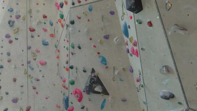 AERIAL: Aerial view of the high walls of a climbing gym filled with colorful magnesium-covered holds. Flying around an empty indoor rock-climbing training center closed due to the covid-19 outbreak.