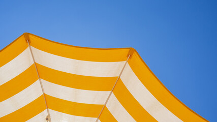 White and yellow striped beach umbrella. Blue sky in the background. View from below. Relaxing context. Summer holidays by the sea. General contest and location © Matteo Ceruti