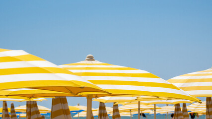 White and yellow striped beach umbrellas. Blue sky. Relaxing context. Summer holidays at the sea. General contest and location © Matteo Ceruti