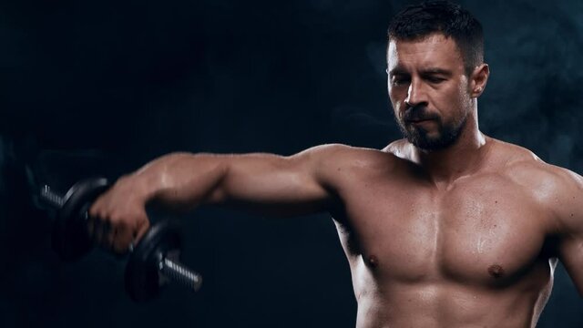 Fit and sporty bodybuilder over black background. Bodybuilder training using dumbbells. Sport and fitness.