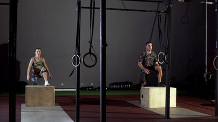 Athletic man and woman does set of box jumps at a crossfit gym