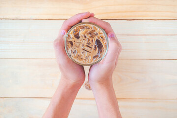 Top view of a man's hand holding a glass of iced coffee on the wooden table, Iced coffee on background.