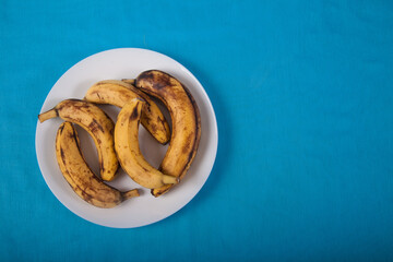 Five ugly bananas lie on a blue porcelain plate on a blue background. copy sraes. Top view.