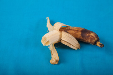 Ugly half-peeled bitten banana on a blue background. Copy spaes.