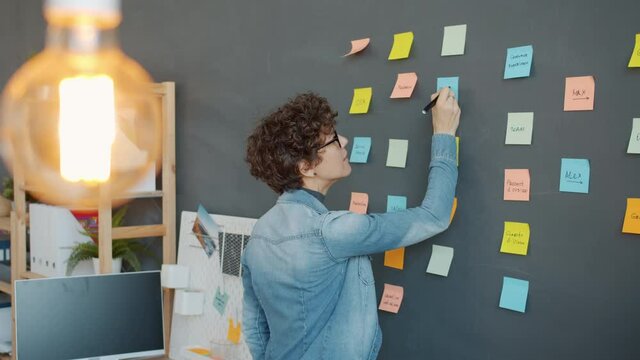 Slow motion of office worker attractive girl writing on bright sticky notes planning marketing strategy in workplace. Creative work and businesspeople concept.