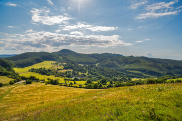 Fototapeta premium Countryside at high noon. Rural scenery with trees and fields on the rolling hills at the foot of the ridge.