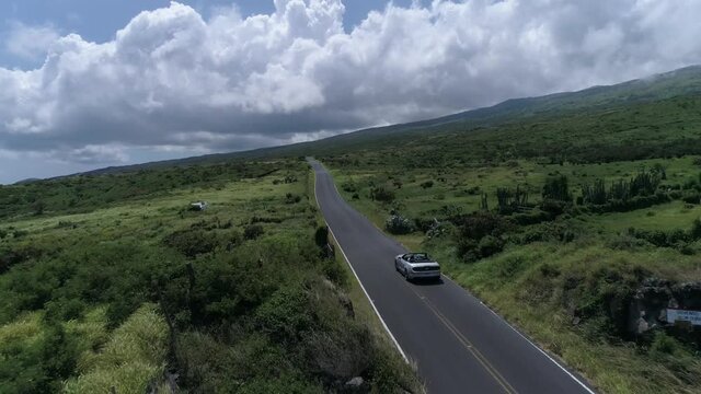 Convertible drives down east Kaupo road towards Kula Maui Hawaii. Aerial drone footage. Green beautiful coastline. 