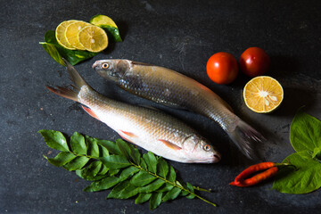 Raw fish on black background along with other condiments.