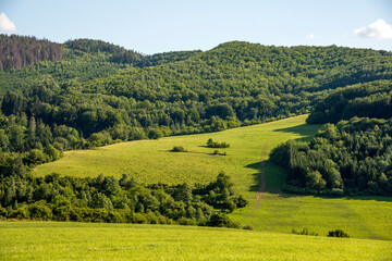 Countryside at high noon. Rural scenery with trees and fields on the rolling hills at the foot of the ridge.