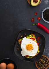 Avocado on toast with poached egg toasted pumpkin seeds, chilli peppers and seasons s with salt and pepper.  Food photography in flat lay style against a dark grey background with space for copy text.
