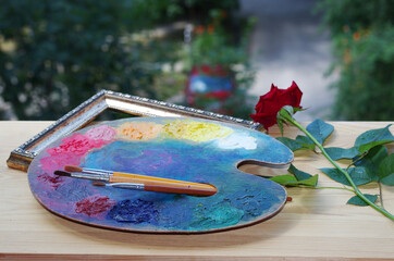 Art palette with brushes and a red rose on the windowsill.