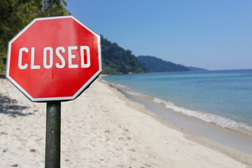 Red closed sign on beach background. Closed facilities because of corona virus. COVID-19 pandemic quarantine.