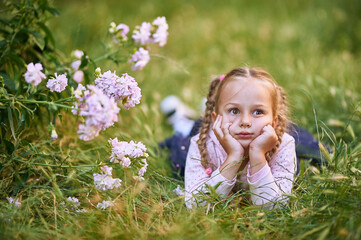 The little girl lies on the grass and holds her head with her hands. Girl makes different facial expressions