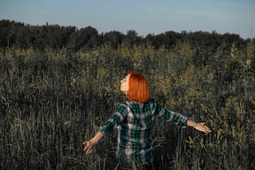 A red haired girl walks through a field of tall grass with her arms open to nature