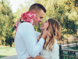 Fototapeta premium The guy kisses the girl in the park, the guy hugs the girl by the face, the couple kisses in the park