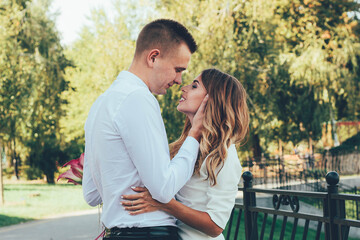Naklejka premium The guy kisses the girl in the park, the guy hugs the girl by the face, the couple kisses in the park