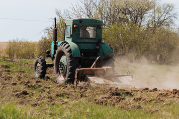 Fototapeta premium An old blue tractor plows a field and cultivates the soil. Agriculture.