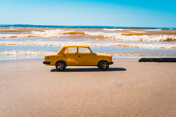 Togliatti / Russia - 12 July 2020: Yellow retro car plastic Russian made AVTOVAZ and metal toy model simulates movement on the sand along the Volga river