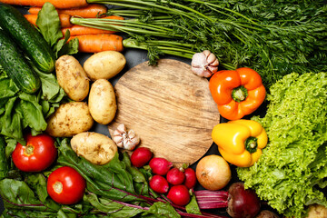 Frame made of fresh assorted vegetables around wooden round cutting board close up