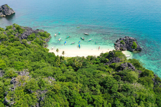 Rocky island with a white sandy beach, top view. Aerial top view of ocean waves, beach and rocky coastline and beautiful forest. Caramoan Islands, Matukad , Philippines.