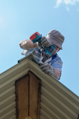 a man works on the roof, attaches the visor with a drill and screws