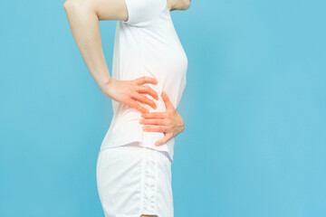 low body of human feels waist pain wearing white clothes standing over isolated blue background,...