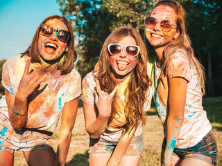Three happy beautiful girls making party at Holi colors festival in summer time.Young smiling women friends having fun after music event at sunset.Positive models going crazy in sunglasses at sunset