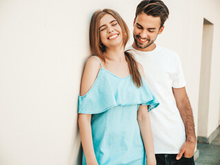 Portrait of smiling beautiful girl and her handsome boyfriend.Woman in casual summer jeans dress.Happy cheerful family.Female having fun.Couple posing in the street near white wall
