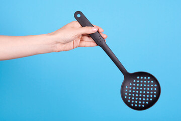 Hand with black plastick ladle utensil. Isolated on blue background.