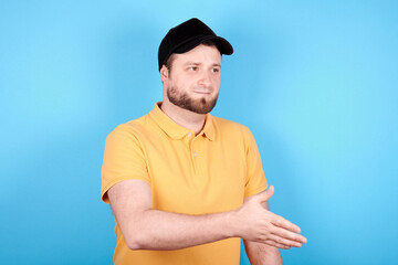 Brunette man holds out his hand, greeting gesture. Isolated on blue background.