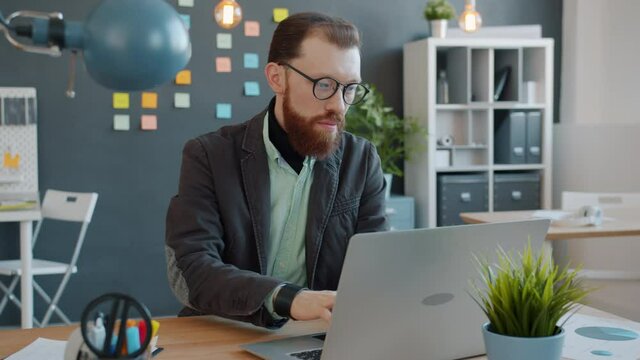 Slow motion of serious young businessman working with laptop computer in modern office typing looking at screen. People, workplace and business concept.