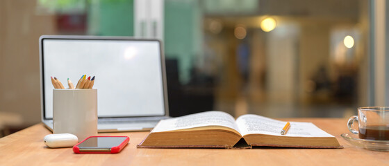 Study table with opened book, mock up laptop, smartphone, stationery and coffee cup
