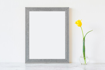 Fresh, beautiful yellow tulip in glass vase on table at light gray wall. Empty place for...
