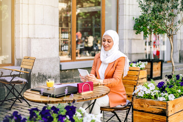 Beautiful young arabic girl in hijab working at street cafe.