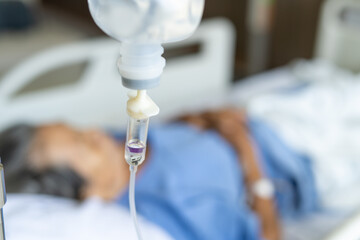 A close-up of a saline bottle strapped to a needle pricked at the hand of a female patient lying in a hospital bed. Medical and treatment of patients concepts