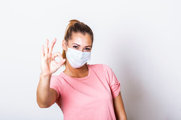 Young woman wearing medical face mask, studio portrait. Woman Wearing Protective Mask and Showing OK sign. Woman wearing surgical mask for corona virus