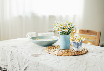 Table with flowers chamomile on linen tablecloth in living room, bright interior. Cottagecore...