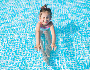 A funny little girl swims in a pool with clear blue water in a yellow lifebuoy in Sunny weather. The concept of rest, travel.