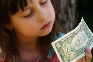 Cute little child girl with US Dollar bill as symbol of financial education. Selective focus on money.