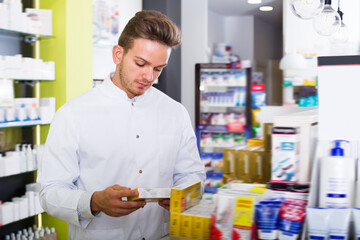 Glad man pharmacist wearing white coat standing among shelves in drug store