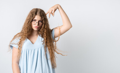 Photo of Pensive girl with curly long hair, and in round spectacles, looking up having pensive expression and holding her hand near head. Isolated over white background. Copy space for your text