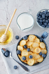 Blue Bowl of mini pancake cereal with blueberries, maple syrup and milk on concrete background. Tiny pancakes, new food trend concept. Cute healthy breakfast or snack. Recipe, menu.