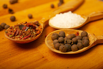 Black allspice, coarse salt and various ground spices in wooden spoons on a wooden Board. Close up.