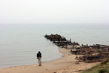 Olkhon / Russia - 27 June 2019: An old wooden pier on lake Baikal. Lonly man walk on beach on Olkhon island. Beautiful landscape with hills and lake. Copy space