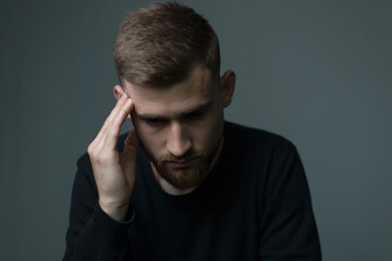 suffering from headache a young bearded guy of about twenty five, in black, presses his hand to his head, suffers from a headache. On a gray background.