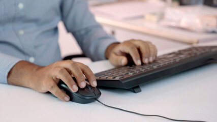 Closeup of Indian businessman typing on keyboard and scrolling mouse at desk in office - Powered by Adobe
