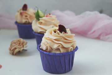 Cupcakes with delicate cream in a lilac stand, decorated with flowers on a white table. Selective focus.