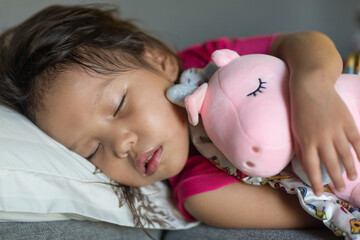 Adorable little asian female child sleeping in bed peacefully while hugging a cute stuffed toy.
